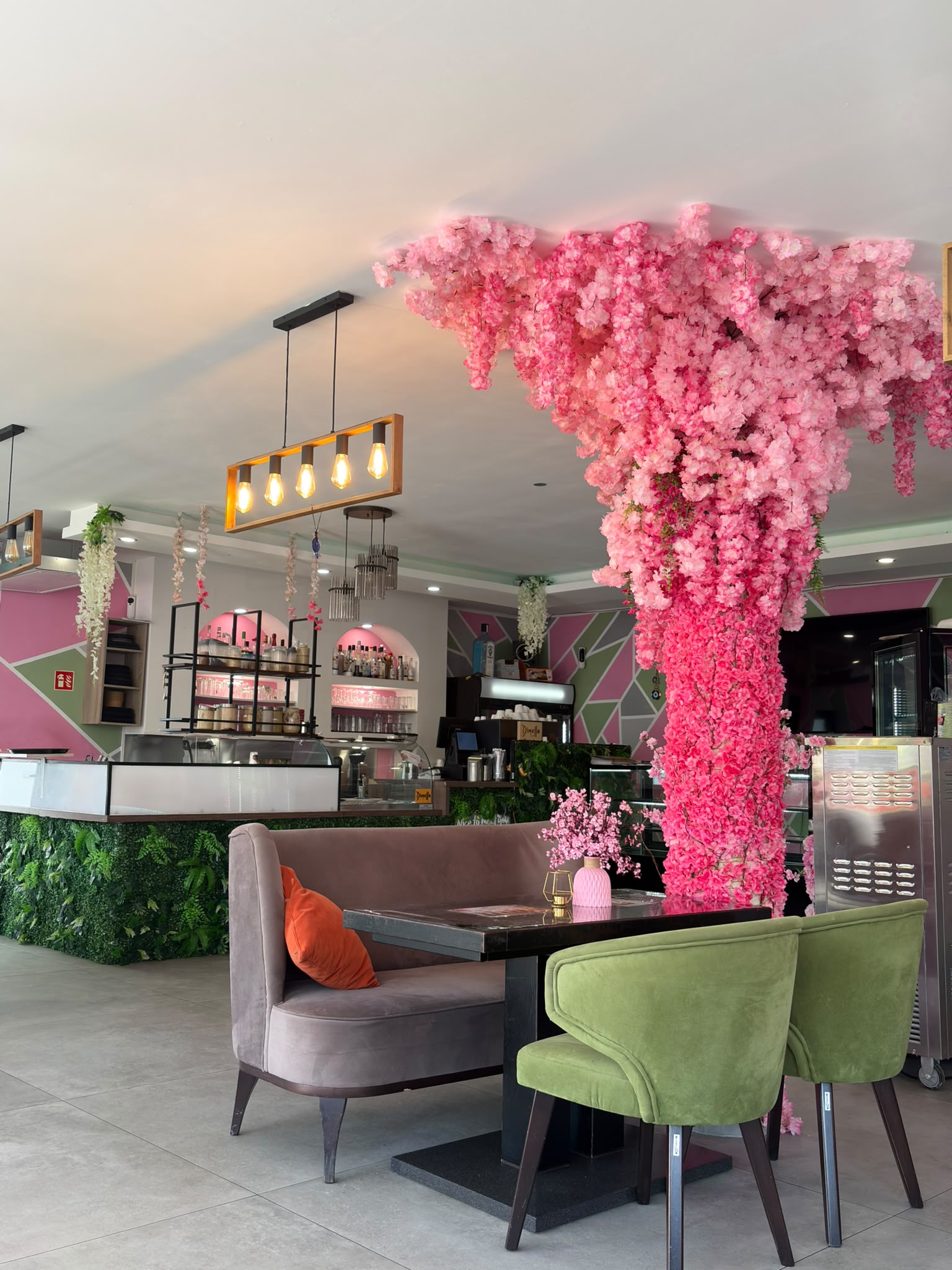 Innenraum des Crêpes House mit pinkem Blütenbaum, Bar und grünen Sesseln